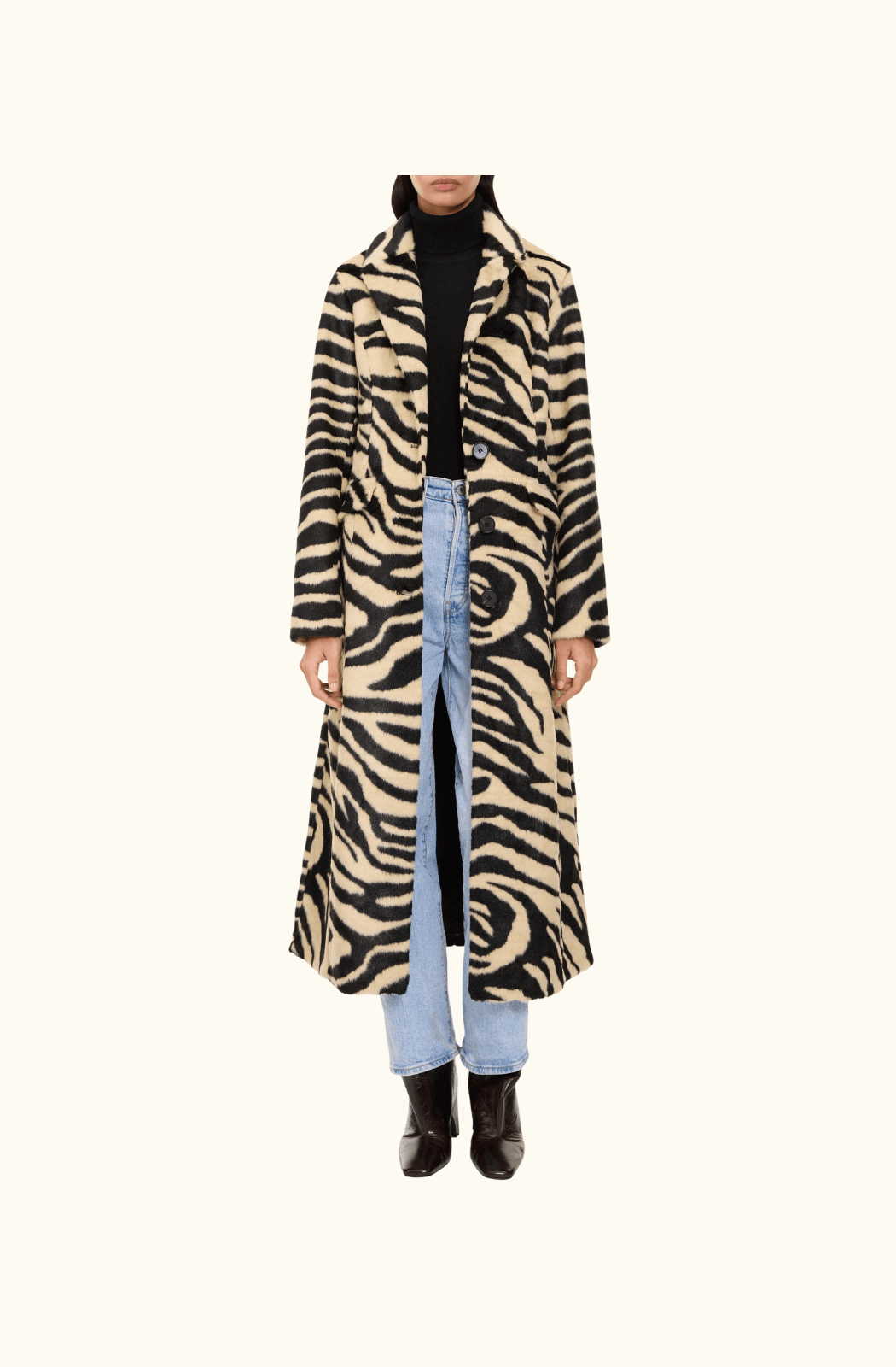 Model wearing the Charlotte Simone 'Nora' zebra print longline coat styled with light blue jeans, a black turtleneck, and dark ankle boots, emphasizing the coat's slim-fit and statement pattern.