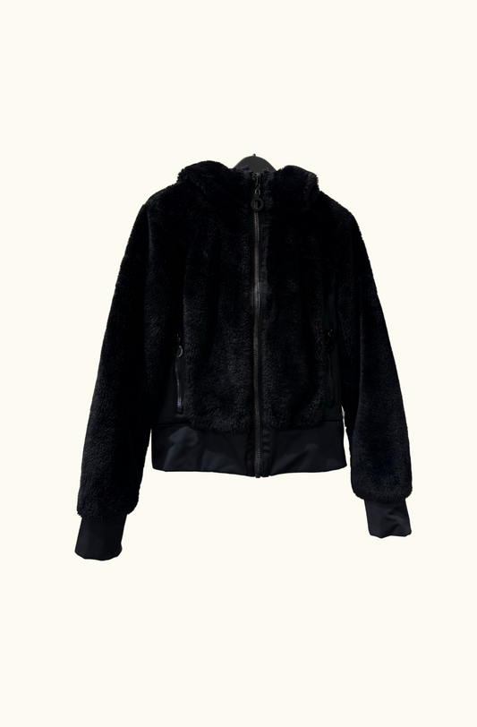 Goldbergh Sunna reversible faux-fur and shell jacket in black, displayed on a hanger against a neutral background. Features a plush faux-fur exterior with a zip-up front and hood.