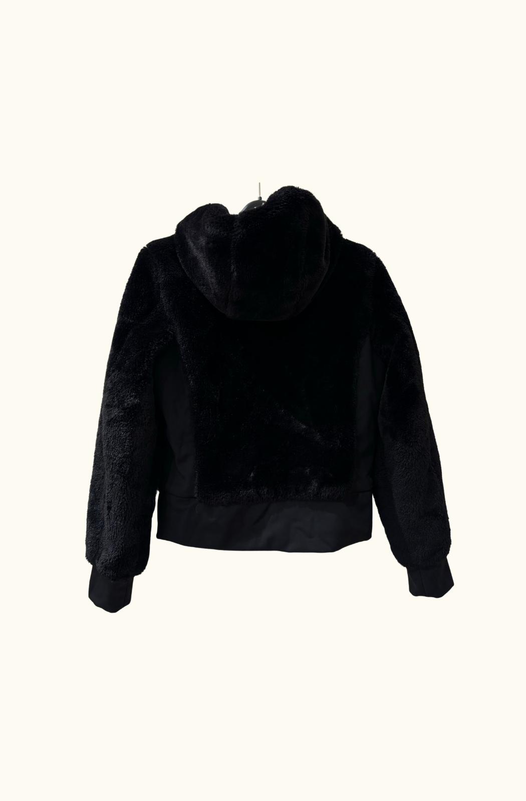 Close-up of the Goldbergh Sunna faux-fur jacket, hanging on a black hanger against a cream wall. The plush texture and zip details are visible.