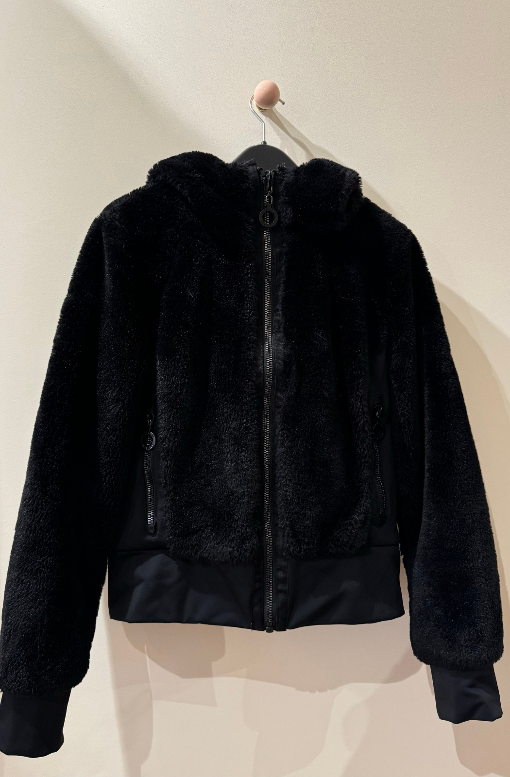 Goldbergh Sunna reversible faux-fur and shell jacket in black, displayed on a hanger against a neutral background. Features a plush faux-fur exterior with a zip-up front and hood.