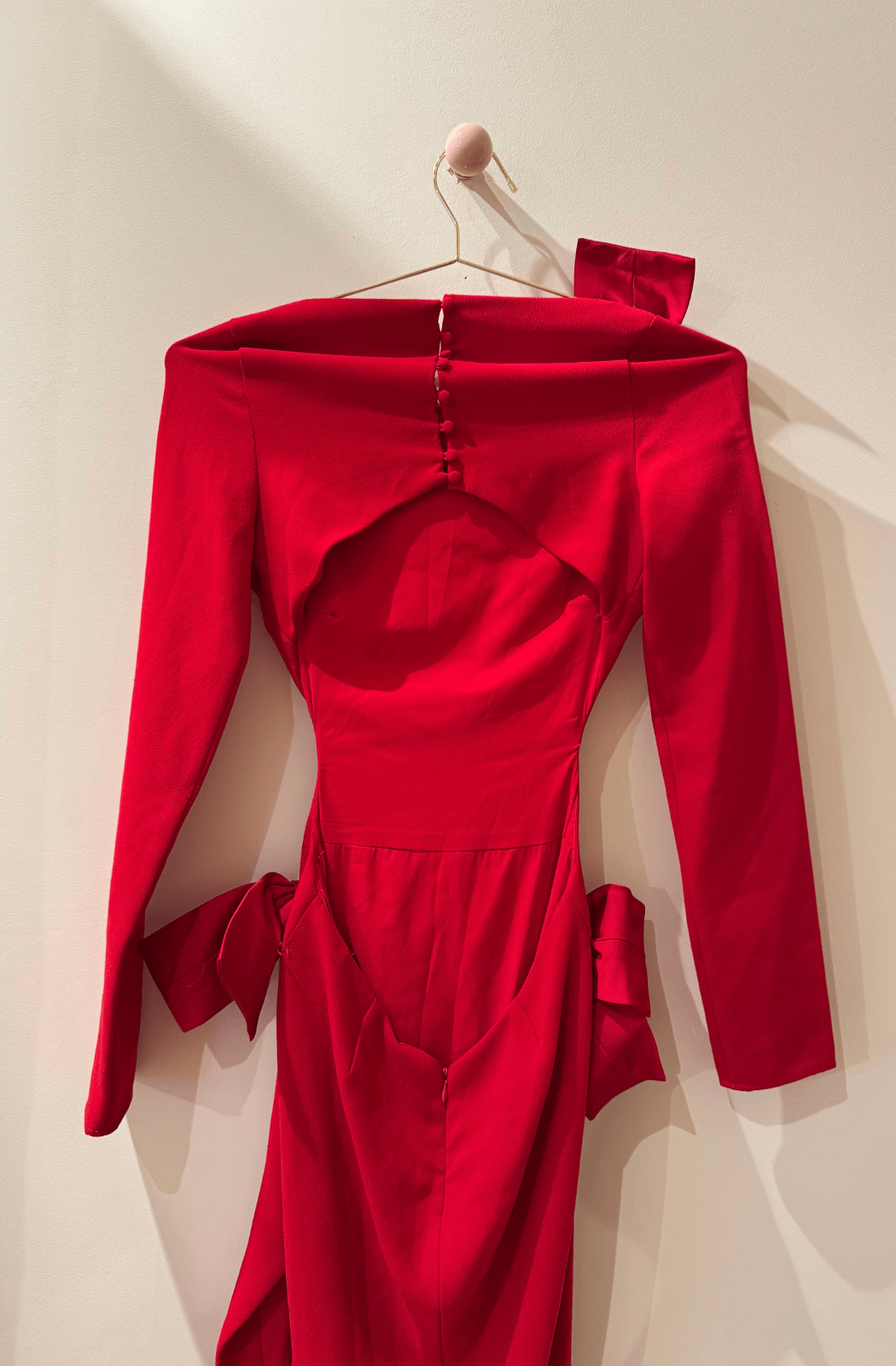 Red open back dress on a hanger against a beige wall