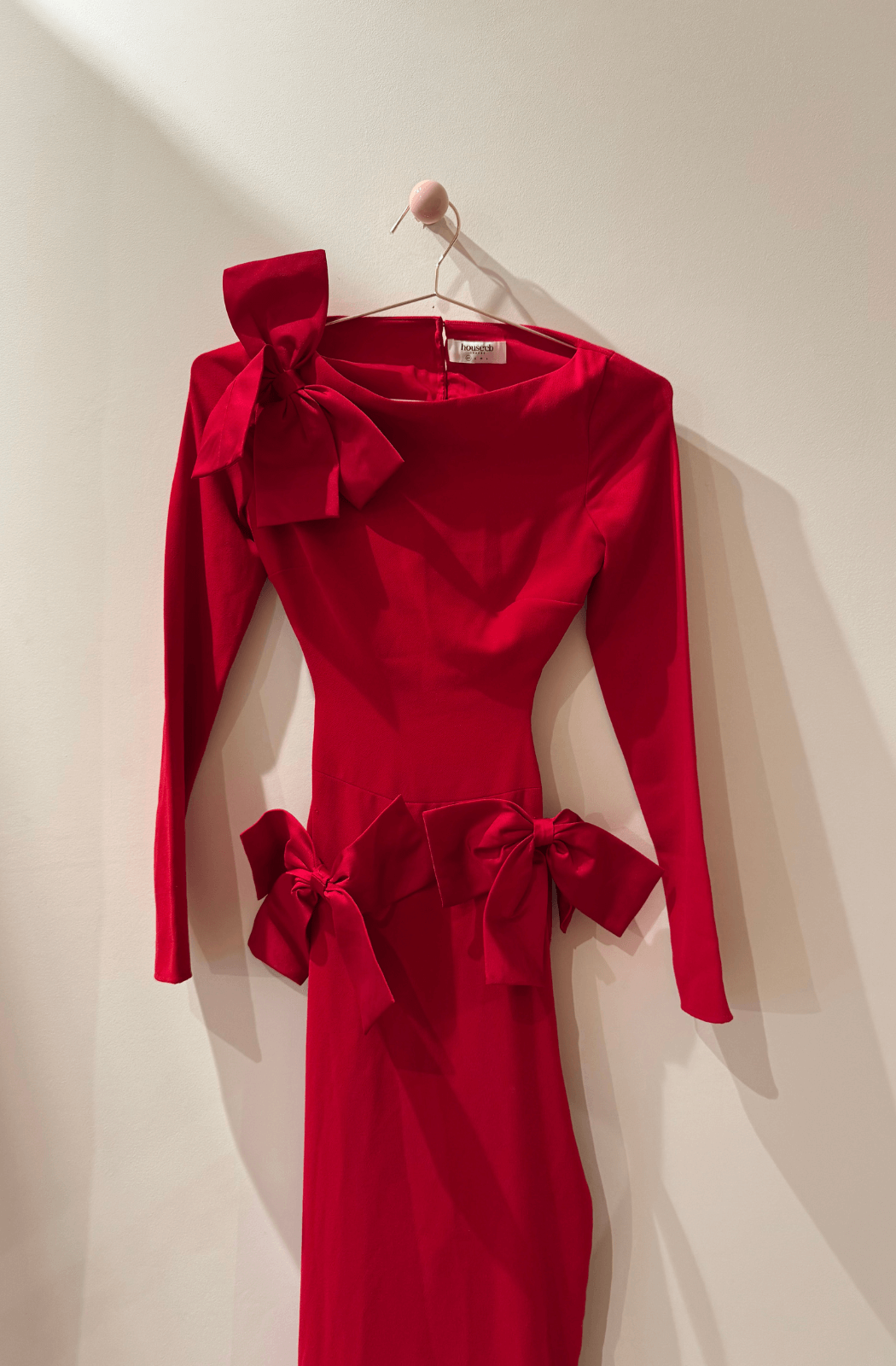 Red dress with bow details on a hanger against a white wall
