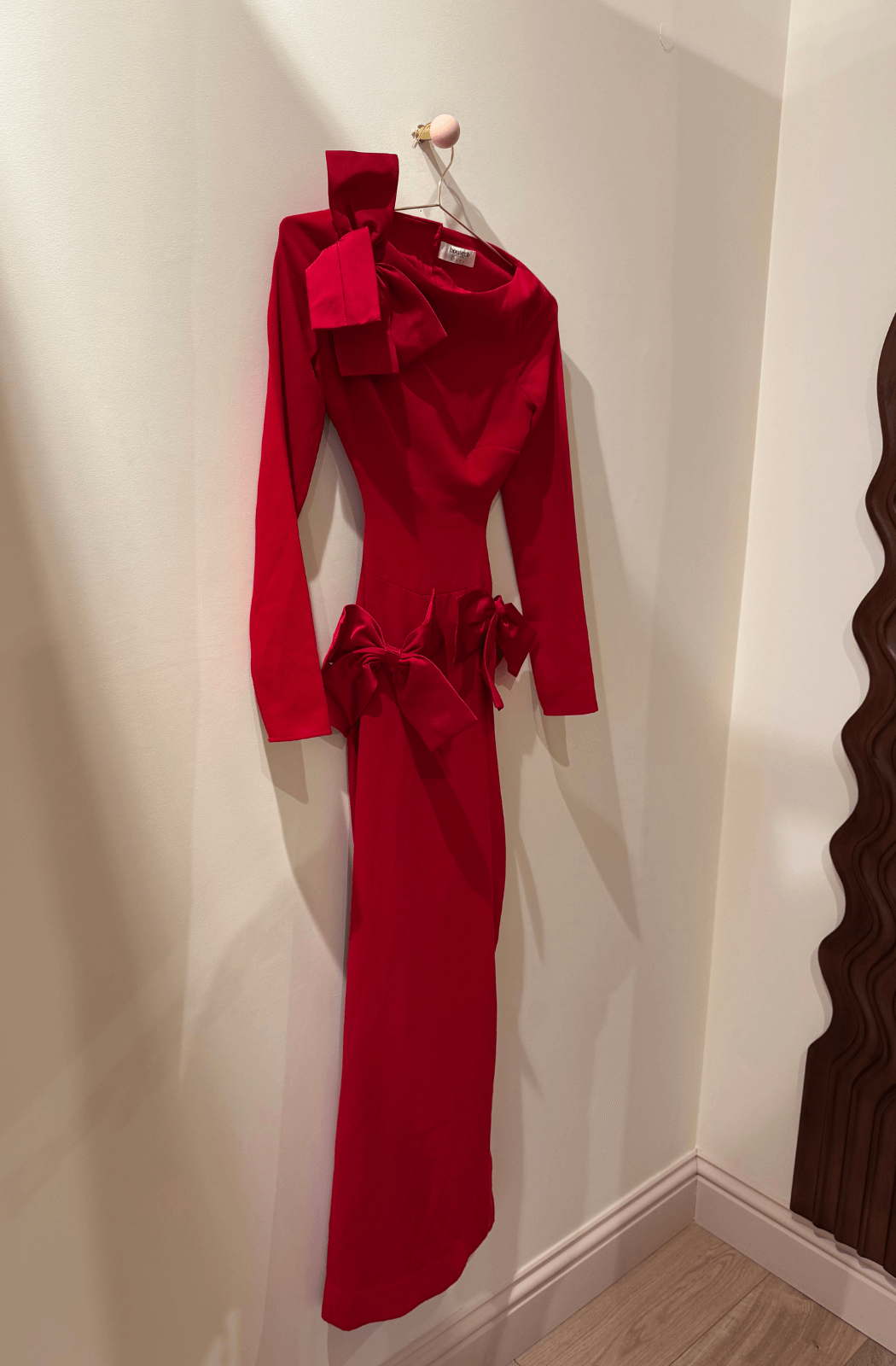 Red dress hanging on a wall in a dressing room with wavy mirror.