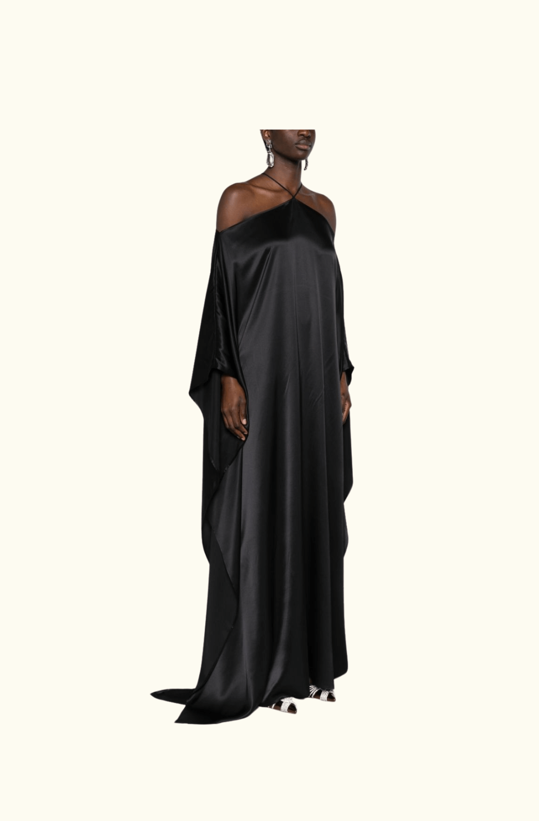 A full side view of the Taller Marmo Sza silk maxi dress being worn by a women, highlighting its luxurious, smooth black silk fabric, halter neckline, and dramatic off-the-shoulder cut with a floor-length hemline.